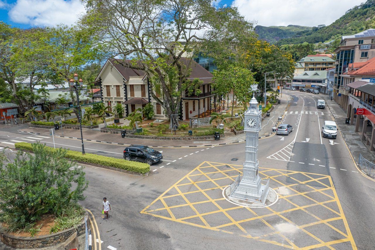 Aerial view of a clock tower at a street intersection surrounded by lush trees and colonial buildings.